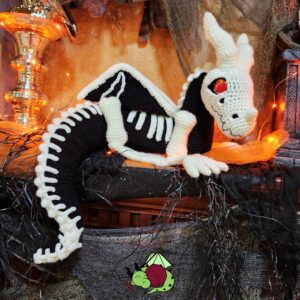 crochet skeleton dragon amigurumi sitting on a shelf, his tail hanging over the edge